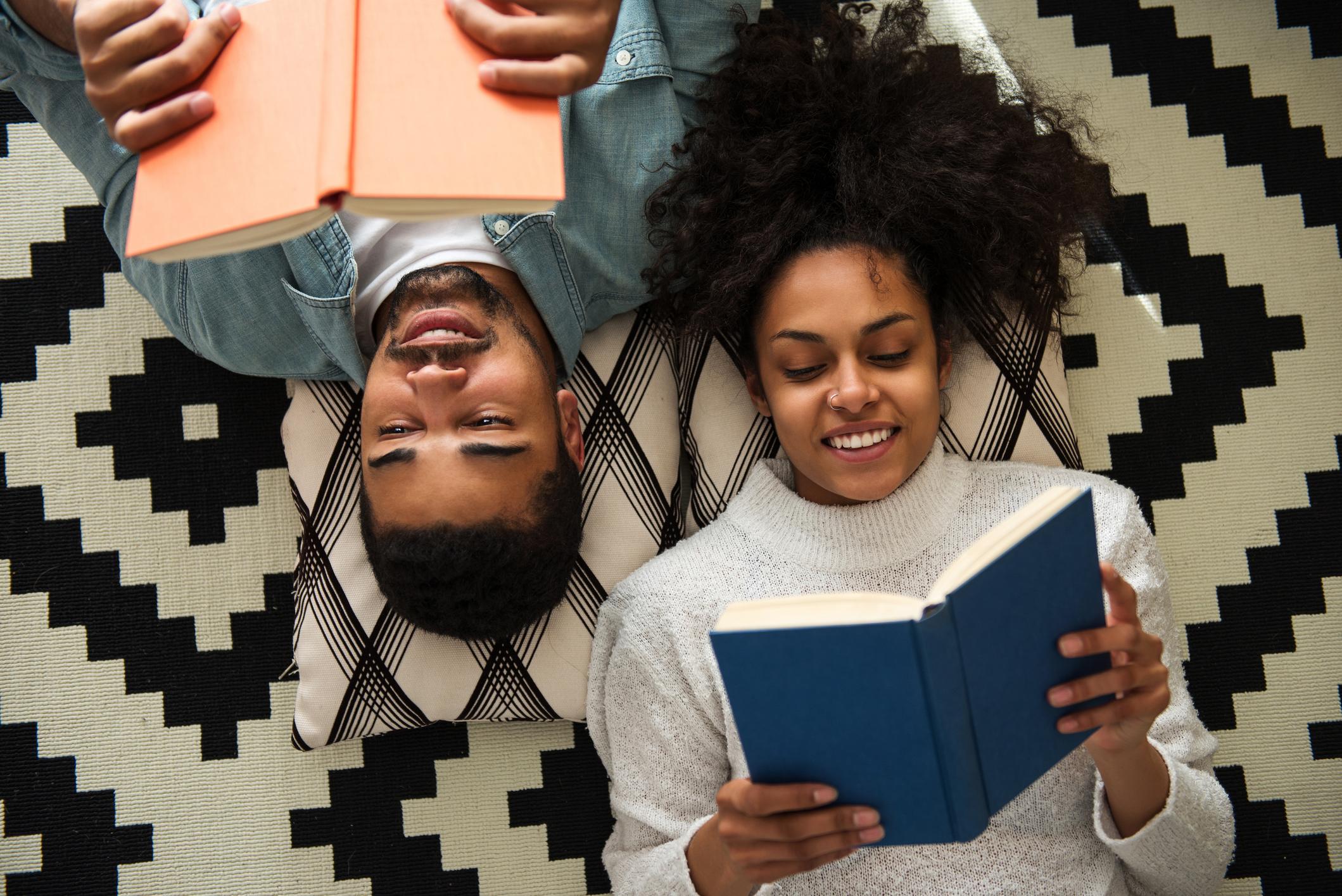 Two people lay next to each other as they read their books.