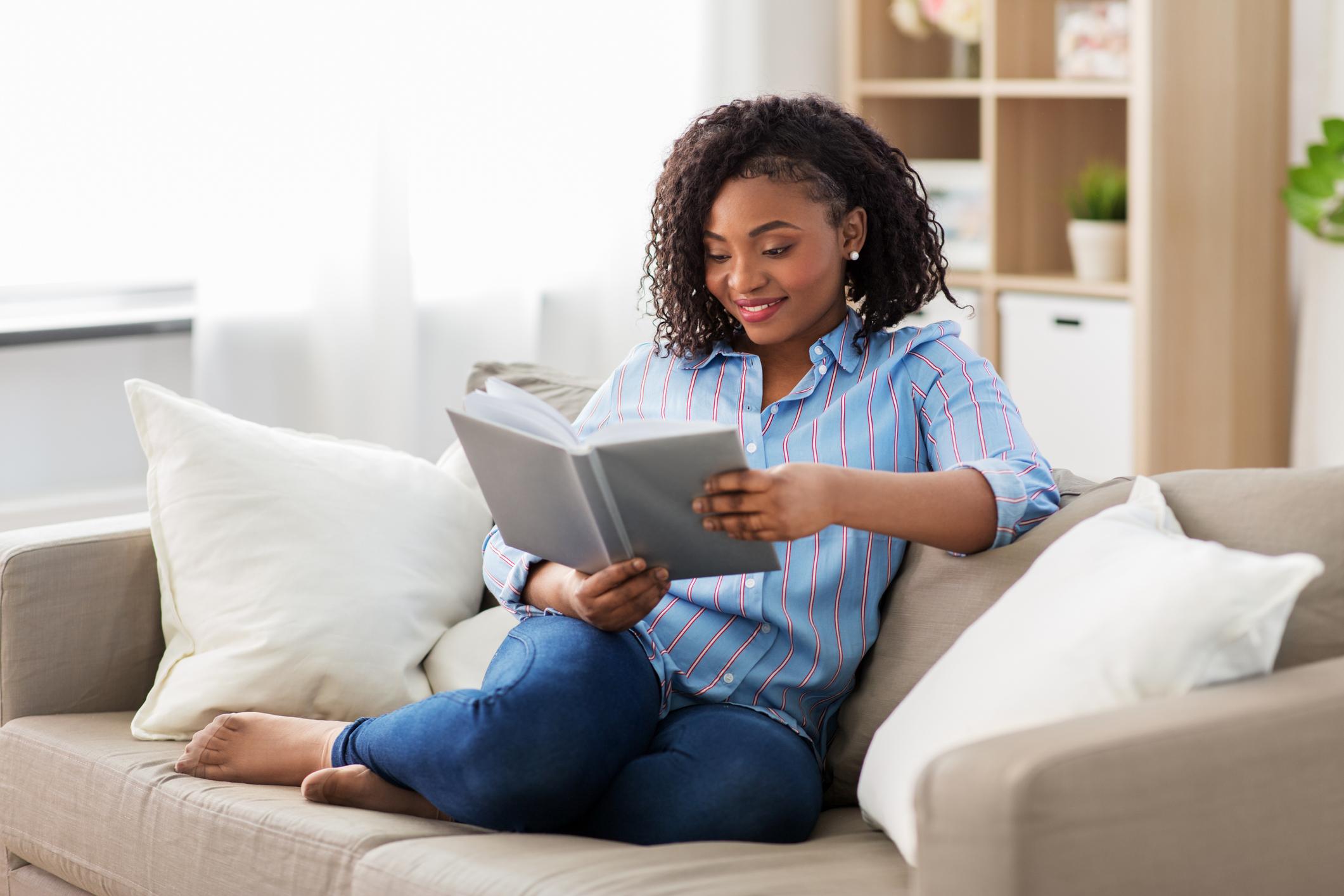 A woman reads a book on a beige sofa.